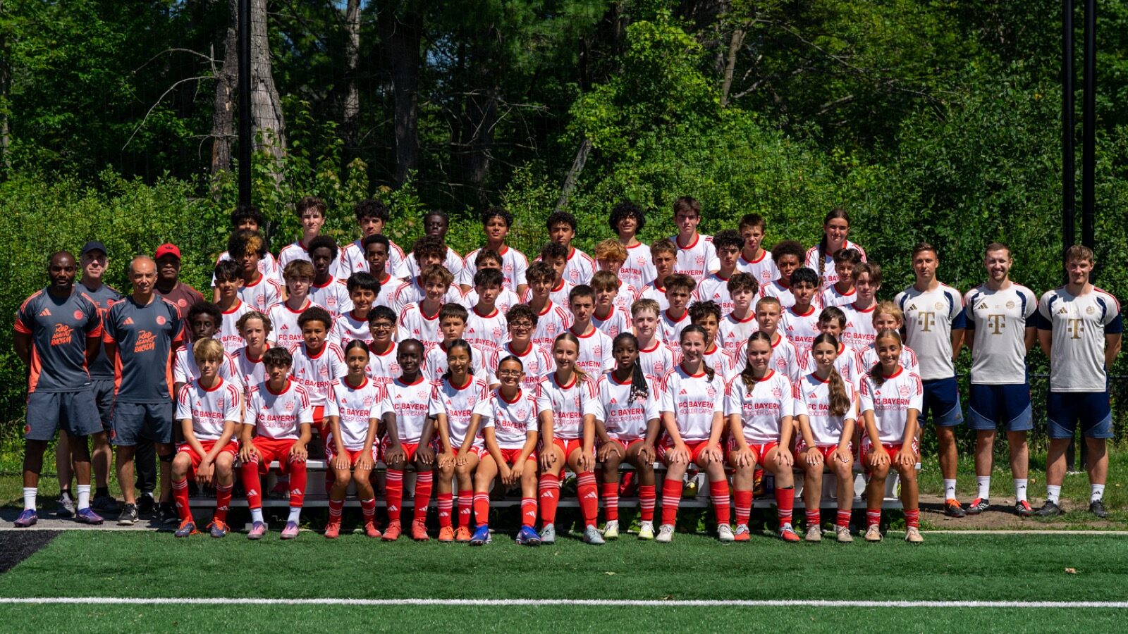 Participants and coaches from the FC Bayern soccer camp at Nepean Hotspurs, in matching red and white kit, posed together on a turf field.