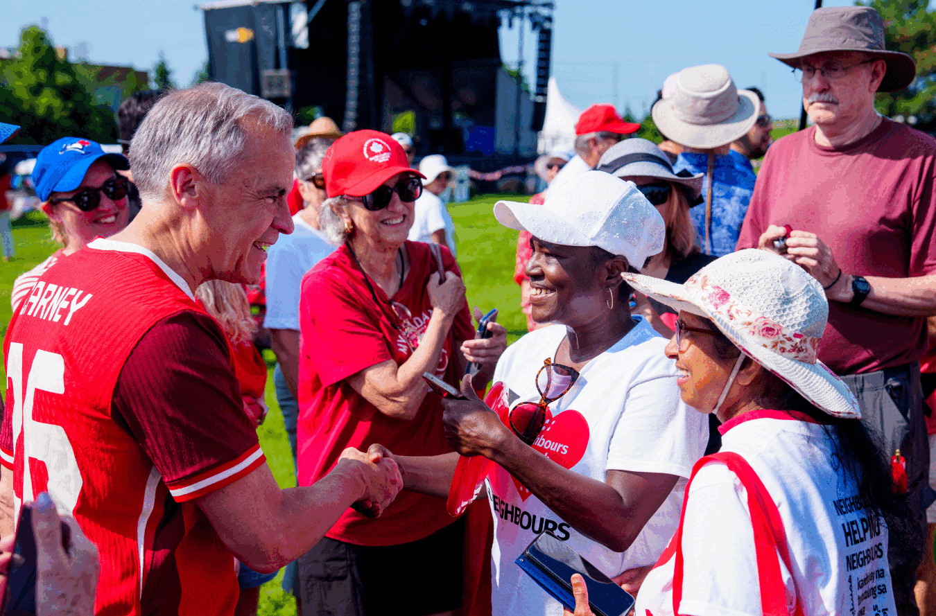 Mark Carney shakes hands with residents in red-and-white Canada Day clothing at the Clarke Fields Park celebration.